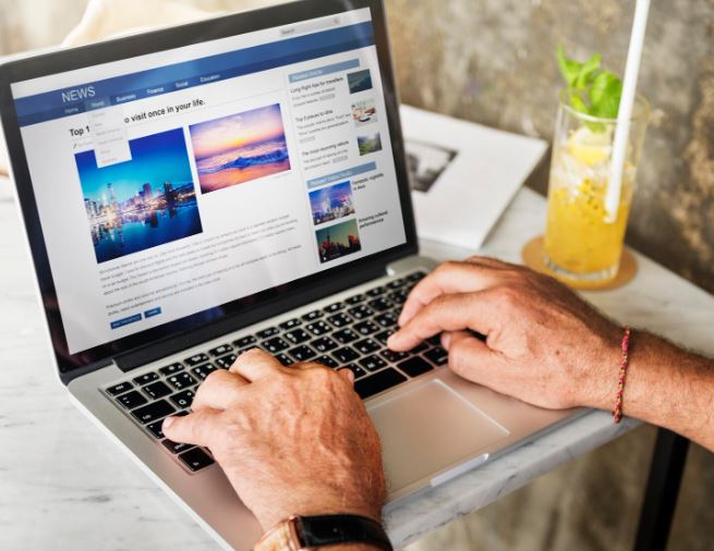Pessoa utilizando um laptop em uma mesa, visualizando um portal de not&iacute;cias no navegador, ilustrando a presen&ccedil;a digital e a cria&ccedil;&atilde;o de conte&uacute;do em sites pr&oacute;prios para estrat&eacute;gias de marketing digital.